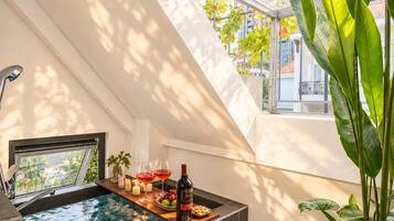 A modern bathroom with a built-in hot tub, a window with a view of a cityscape, and a plant on the right.