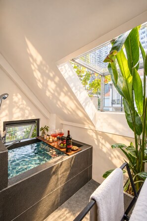 A modern bathroom with a built-in hot tub, a window with a view of a cityscape, and a plant on the right. - Nexus House Thao Dien (Ho Chi Minh City)