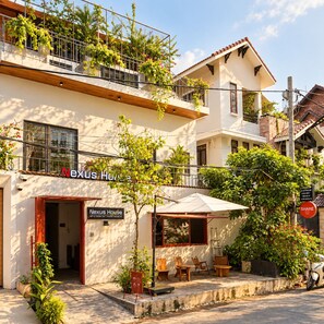 A two-story building with a sign reading 'Nexus House.' There is a balcony with plants and a small outdoor seating area with tables and chairs. - Nexus House Thao Dien (Ho Chi Minh City)