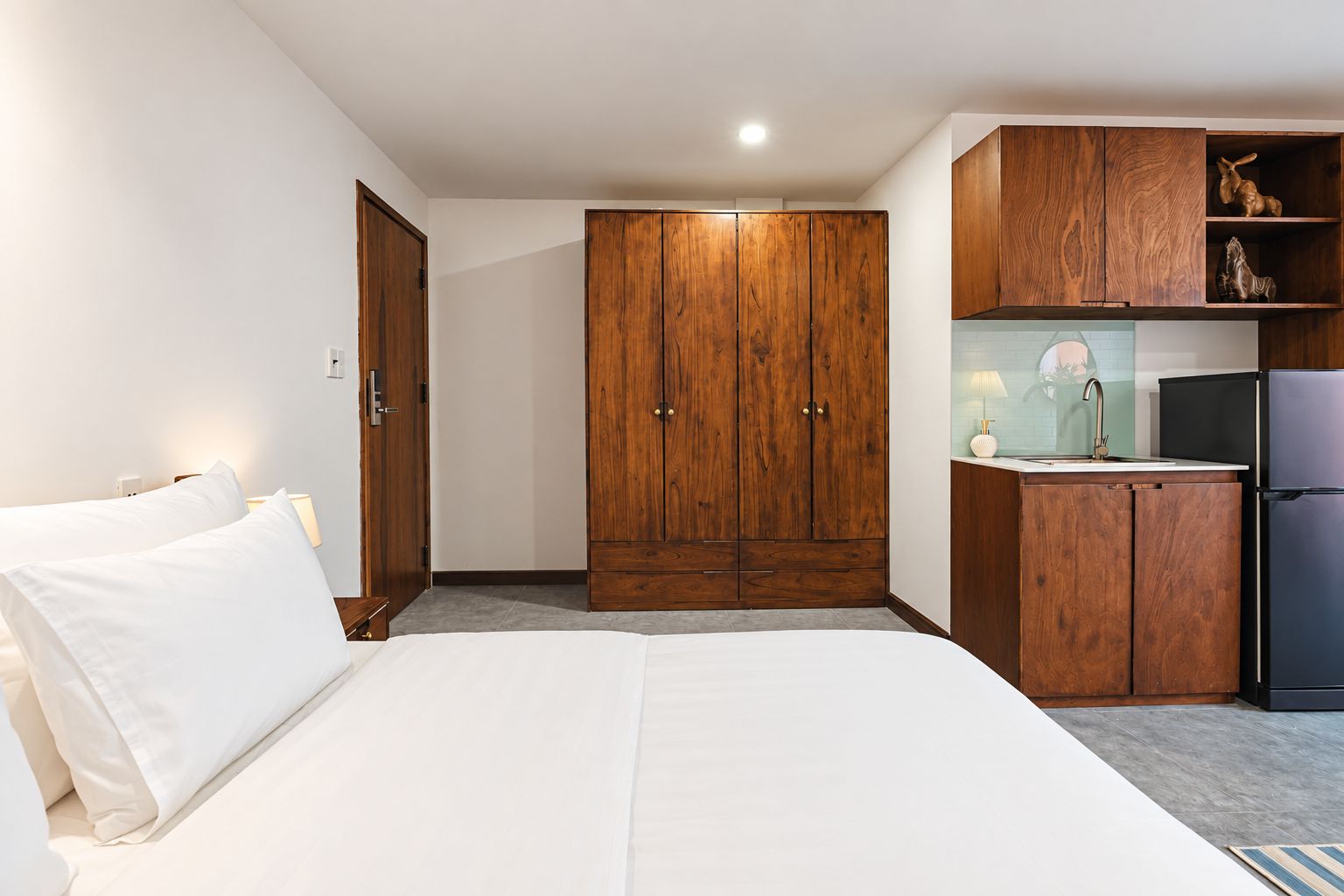 A hotel room with a bed, wooden wardrobe, and a kitchenette.