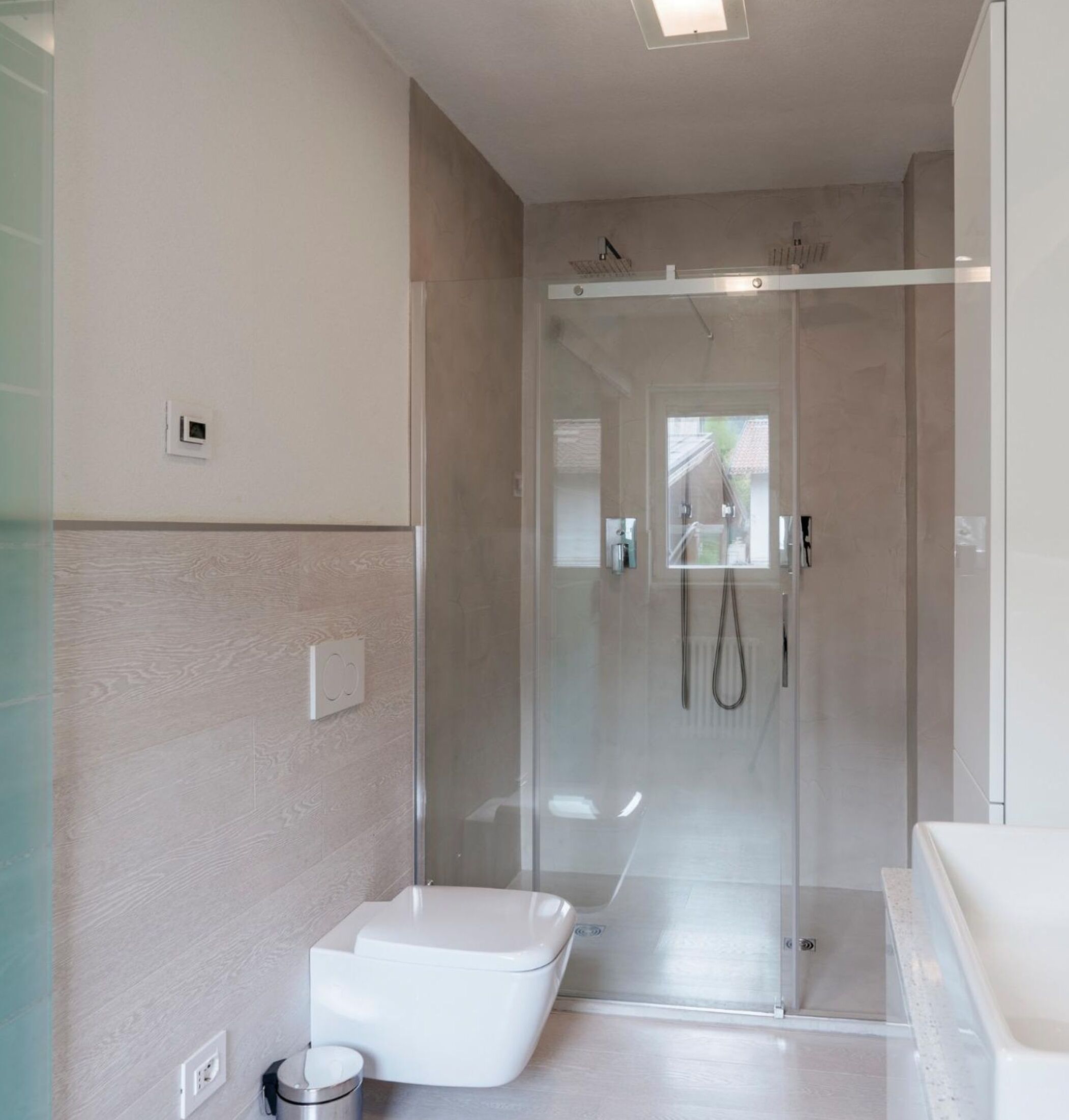 A modern bathroom with a glass-enclosed shower, a white toilet, and a visible window.