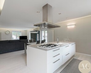 A modern kitchen with a central island, white cabinetry, and a stainless steel range hood. - Snowhite in Incudine (Incudine)