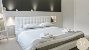 Un dormitorio moderno con una cama grande, una mesita de noche, un estante en la pared y una lámpara en el techo.