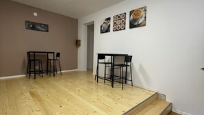 Una habitación amplia con suelo de madera, dos mesas con sillas y una escalera.
