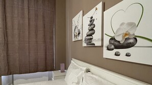 Habitación de hotel con cama, ventana con cortinas y dos obras de arte en la pared que muestran una pila de piedras y una orquídea.