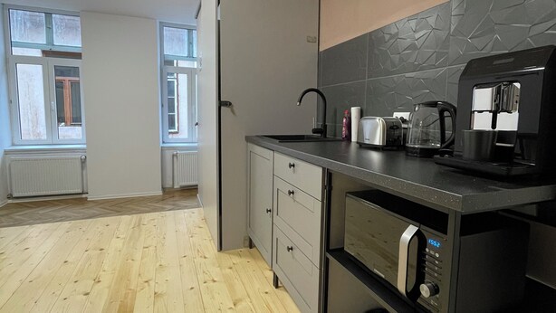 Una cocina moderna con suelo de madera, horno empotrado, cafetera y ventana con vistas al exterior.