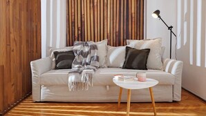 A modern living room with a white sofa, a wooden accent wall, and a small round table. - Lunga 16 Guesthouse in City Center (Brașov)