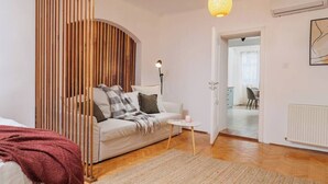 A modern living room with a sofa, a small table, and a lamp. There is a wooden slat partition and a doorway leading to another room. - Lunga 16 Guesthouse in City Center (Brașov)