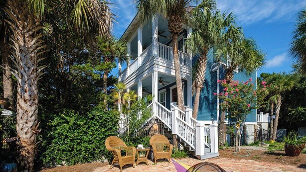 A two-story house with a balcony, surrounded by palm trees and a garden. - Bridges Cottage - Vintage in Heart of Cedar Key! (Cedar Key)