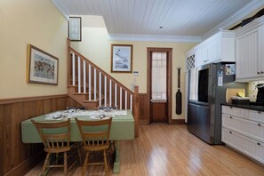 A dining area with a wooden table and chairs, a staircase, and a kitchen with white cabinets and stainless steel appliances. - Bridges Cottage - Vintage in Heart of Cedar Key! (Cedar Key)