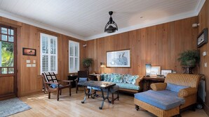 A spacious room with wooden walls and a high ceiling. There is a sofa, a chair, and a small table. - Bridges Cottage - Vintage in Heart of Cedar Key! (Cedar Key)