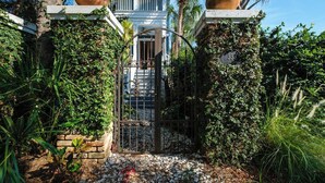 A gated entrance with a metal gate, a brick pathway, and lush greenery. - Bridges Cottage - Vintage in Heart of Cedar Key! (Cedar Key)