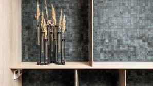 A shelf with vases containing dried plants against a tiled wall.