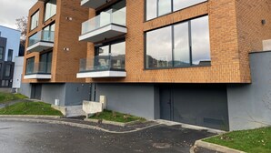 A modern multi-story residential building with balconies, large windows, and a parking area in front.