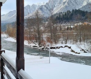 A river with snow-covered banks, a wooden fence, and mountains in the background.