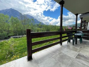 A terrace with a wooden railing, a table with chairs, and a view of a mountain and greenery. - Cozy Riverfront 1 with Garden and Mountain View (Bușteni)