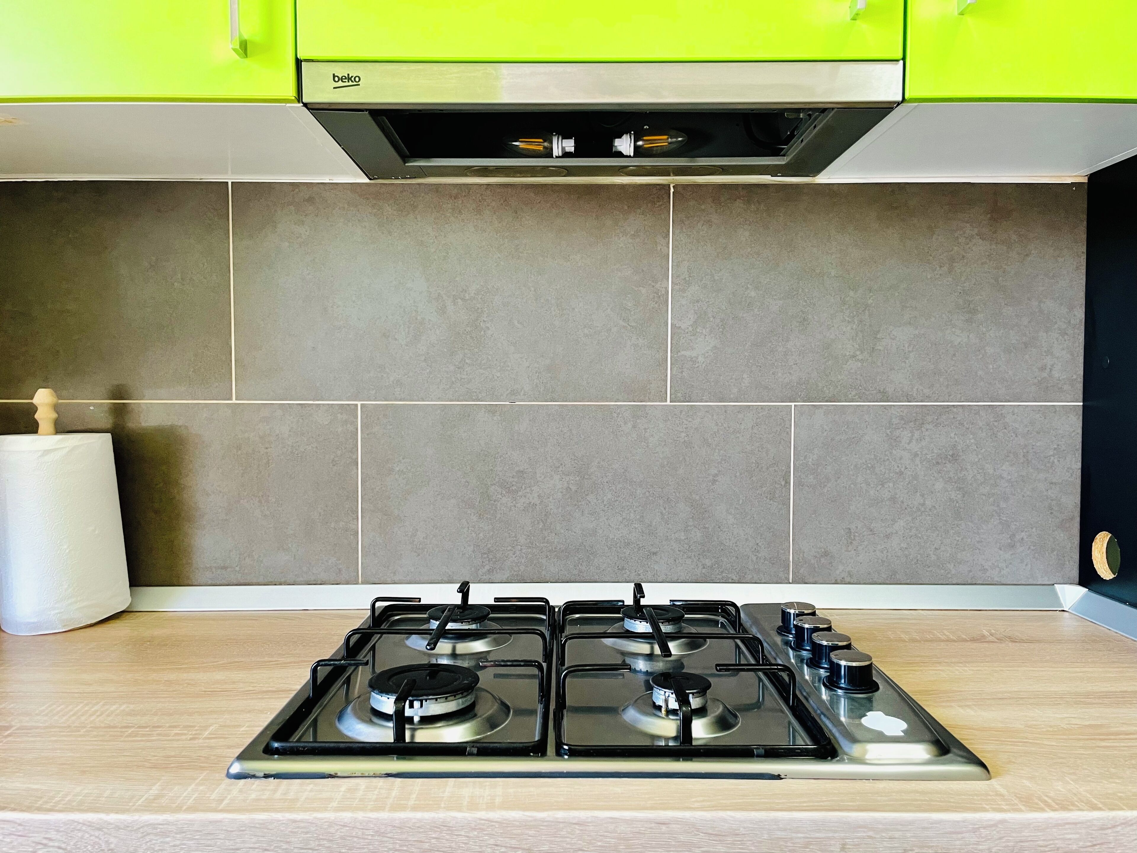 Een keuken met een gasfornuis, een rol keukenpapier en een groen kastje boven het fornuis.