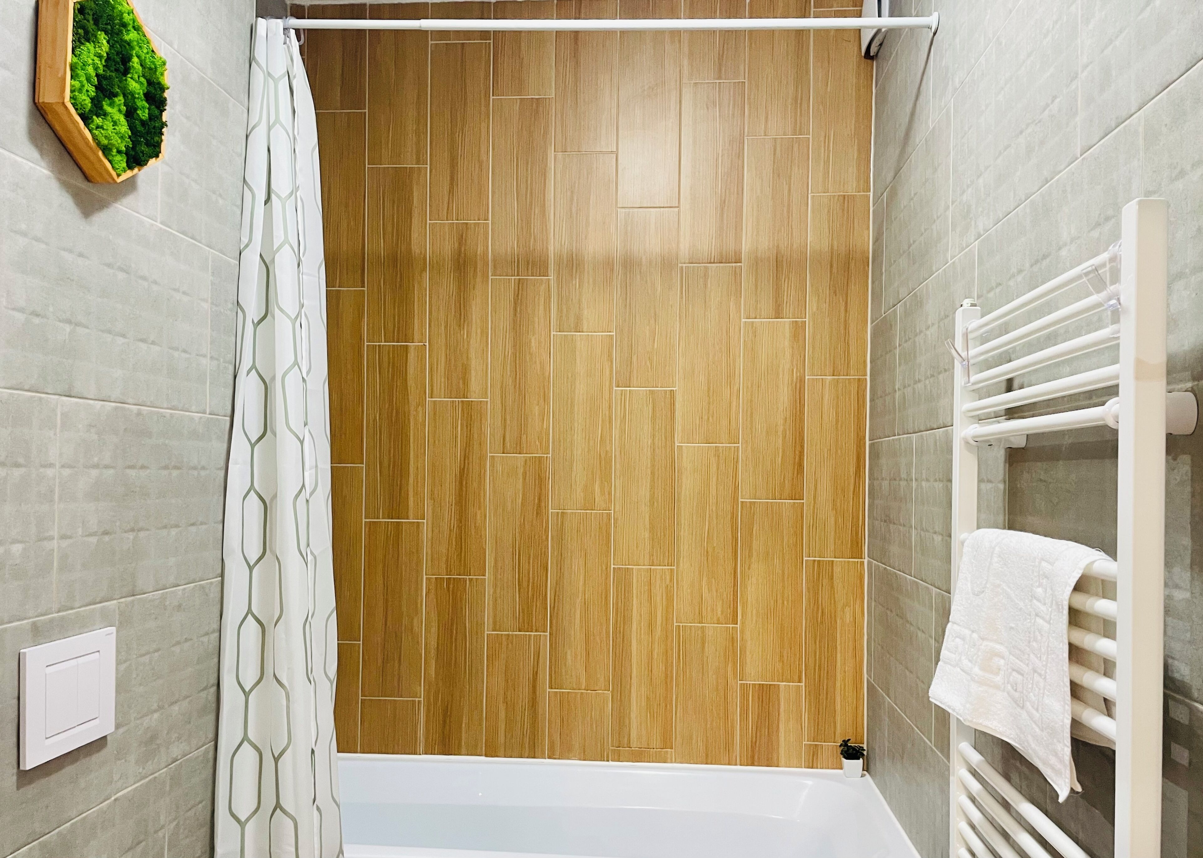 A modern bathroom with a wooden panel wall, a shower curtain with a geometric pattern, and a white towel rack with a towel.