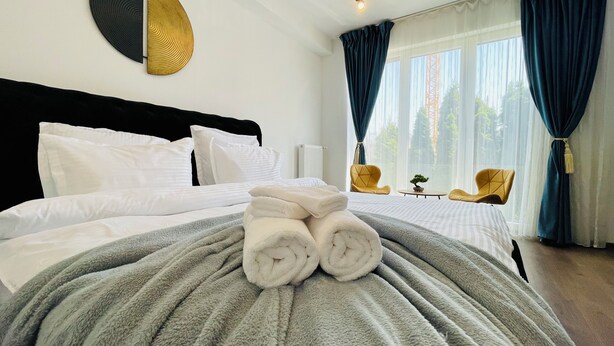 Habitación de hotel con una cama bien hecha, un adorno circular en la pared, una ventana con cortinas y dos sillas junto a la ventana.