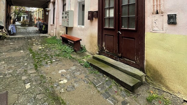 Una estrecha calle adoquinada con un edificio rosa que tiene una gran puerta de madera arqueada y un banco afuera.
