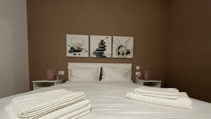 Una cama bien hecha con toallas dobladas, un cabecero blanco y tres obras de arte colgadas en la pared que representan la naturaleza y el equilibrio.