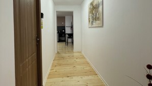 Un pasillo con suelo de madera, una puerta a la izquierda y un cuadro en la pared derecha.