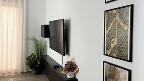 A modern living room with a flat-screen TV mounted on the wall, a dark console table with decorative items, and three framed artworks on the wall. - Scandiland Apartment (Brașov)