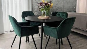 A dining area with a round table, four green upholstered chairs, and a vase of flowers. - Scandiland Apartment (Brașov)