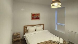 A bedroom with a wooden bed, a bedside table, a hanging light fixture, and a window.