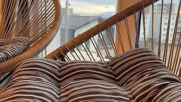 A wicker chair with striped cushions in a room with a view of buildings through a window.