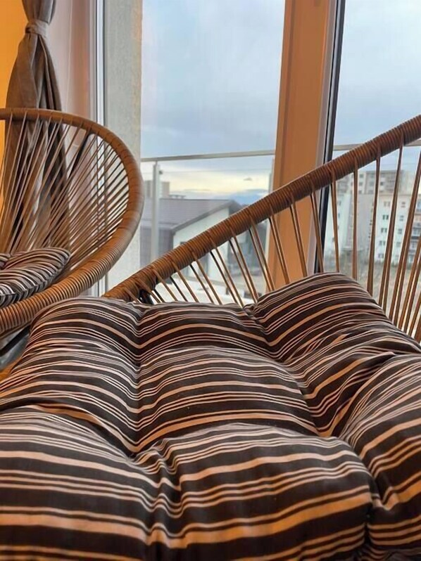 A wicker chair with striped cushions in a room with a view of buildings through a window.