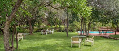 Un espacio al aire libre con césped, piscina, mesas de picnic y sillas.
