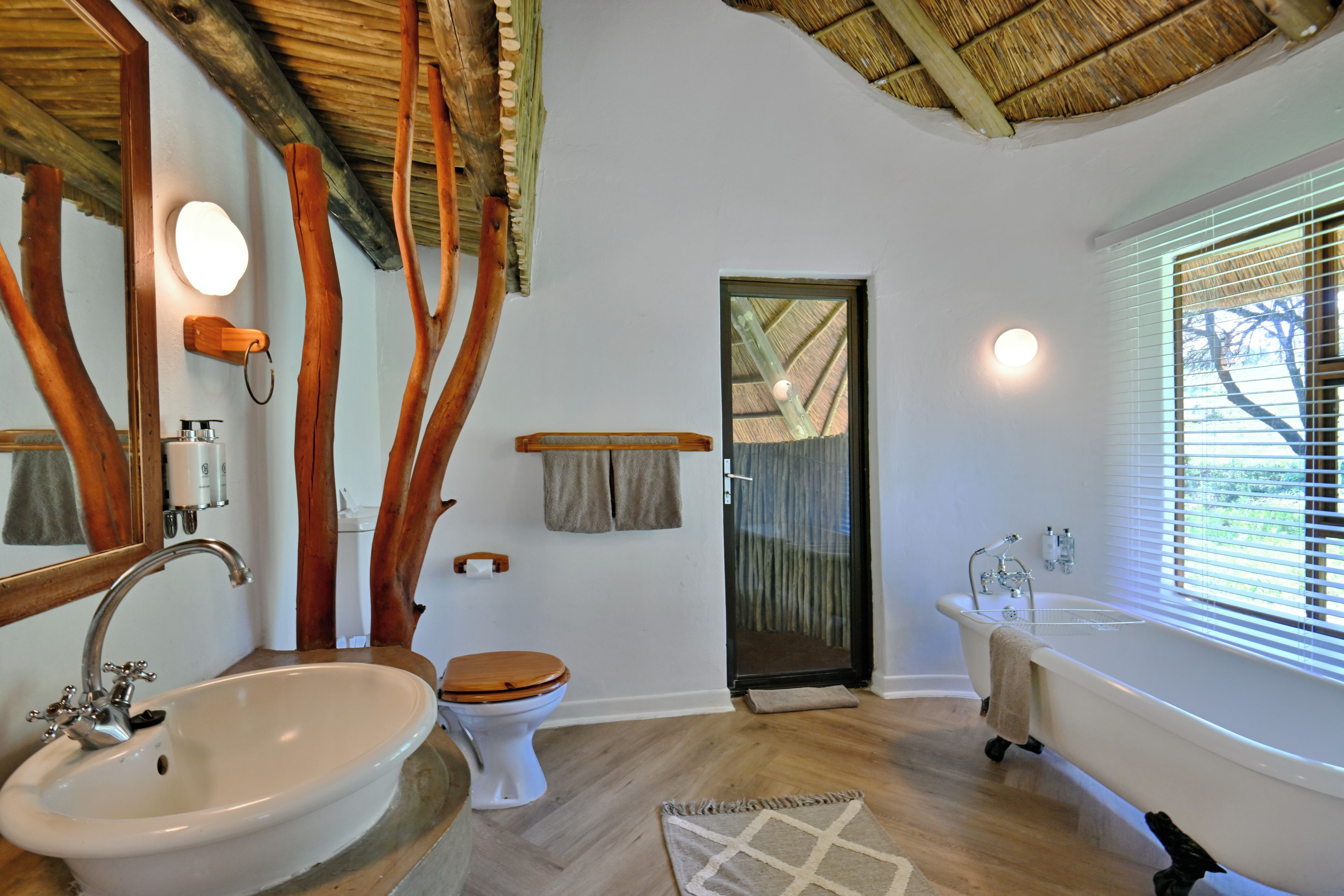 Un baño con techo de madera, un lavamanos blanco, inodoro, bañera y ventana con persianas.