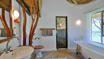 Un baño con techo de madera, un lavamanos blanco, inodoro, bañera y ventana con persianas.