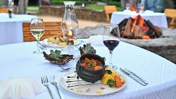 An outdoor dining setting with a table set for a meal, a fire pit in the background, and a bottle of wine.