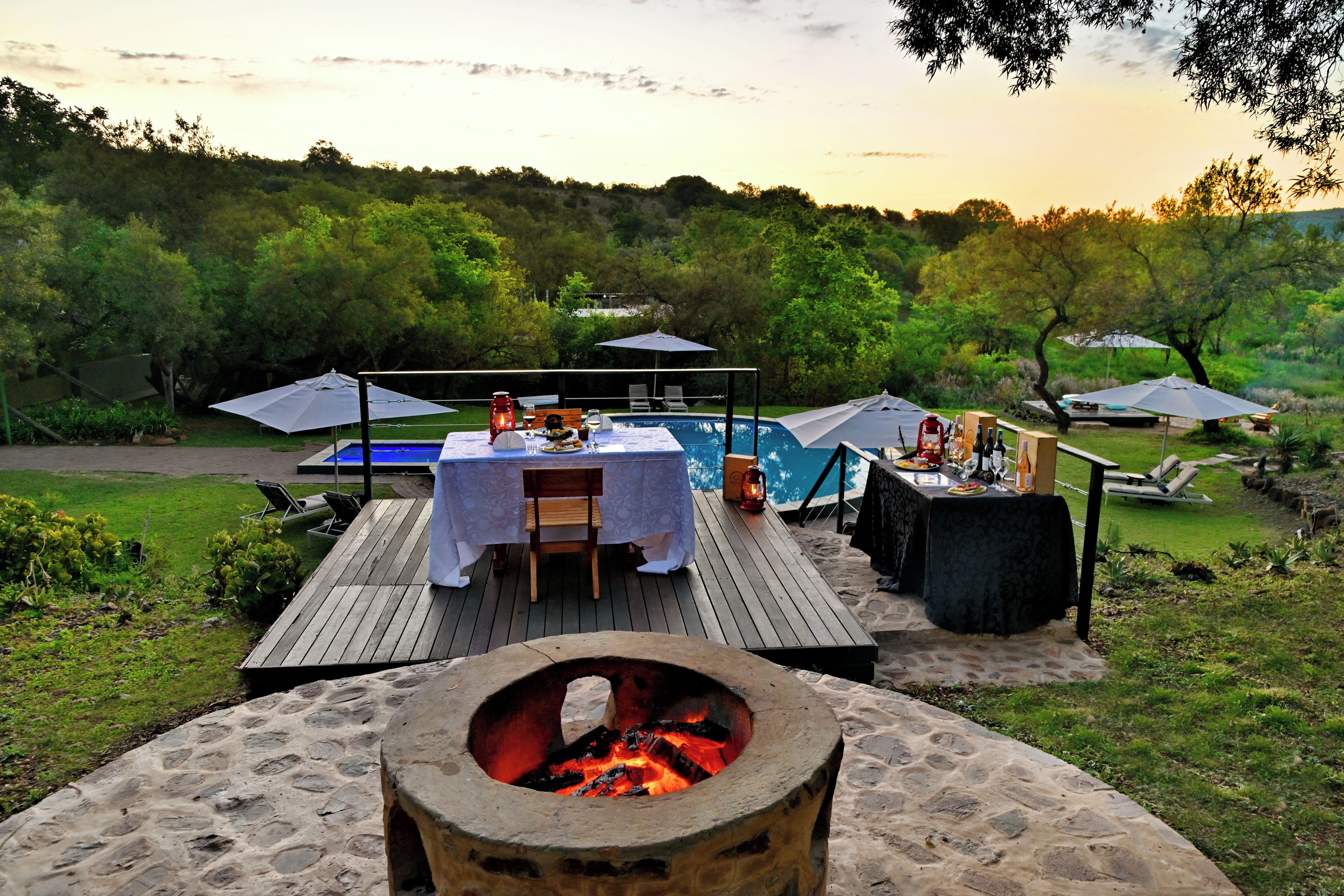 An outdoor dining area with a pool, a fire pit, and lounge chairs.