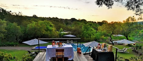 An outdoor dining area with a pool, a fire pit, and lounge chairs.