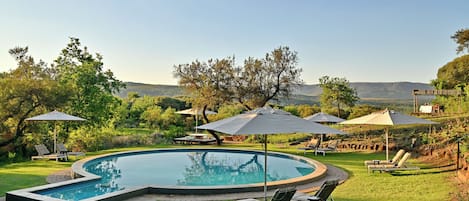 A swimming pool with lounge chairs and umbrellas, surrounded by grass and trees.