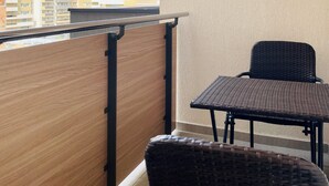 Un balcon doté d’un plancher en bois, de deux fauteuils en osier et d’une rambarde en métal.