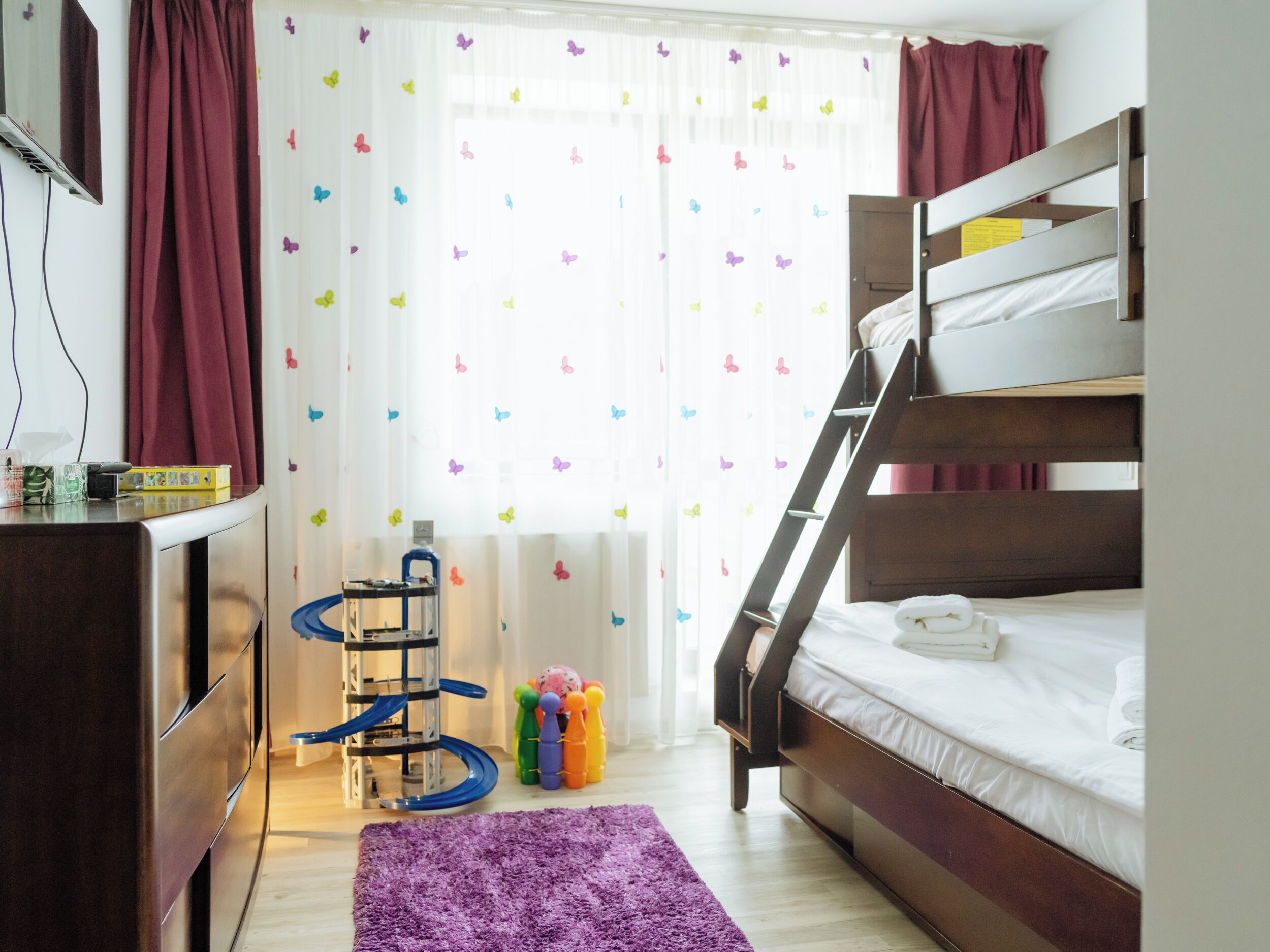 A bunk bed room with a desk, a radiator, and a window with butterfly curtains.