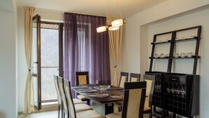Un comedor con una mesa larga, múltiples sillas, una araña y una estantería para vinos.