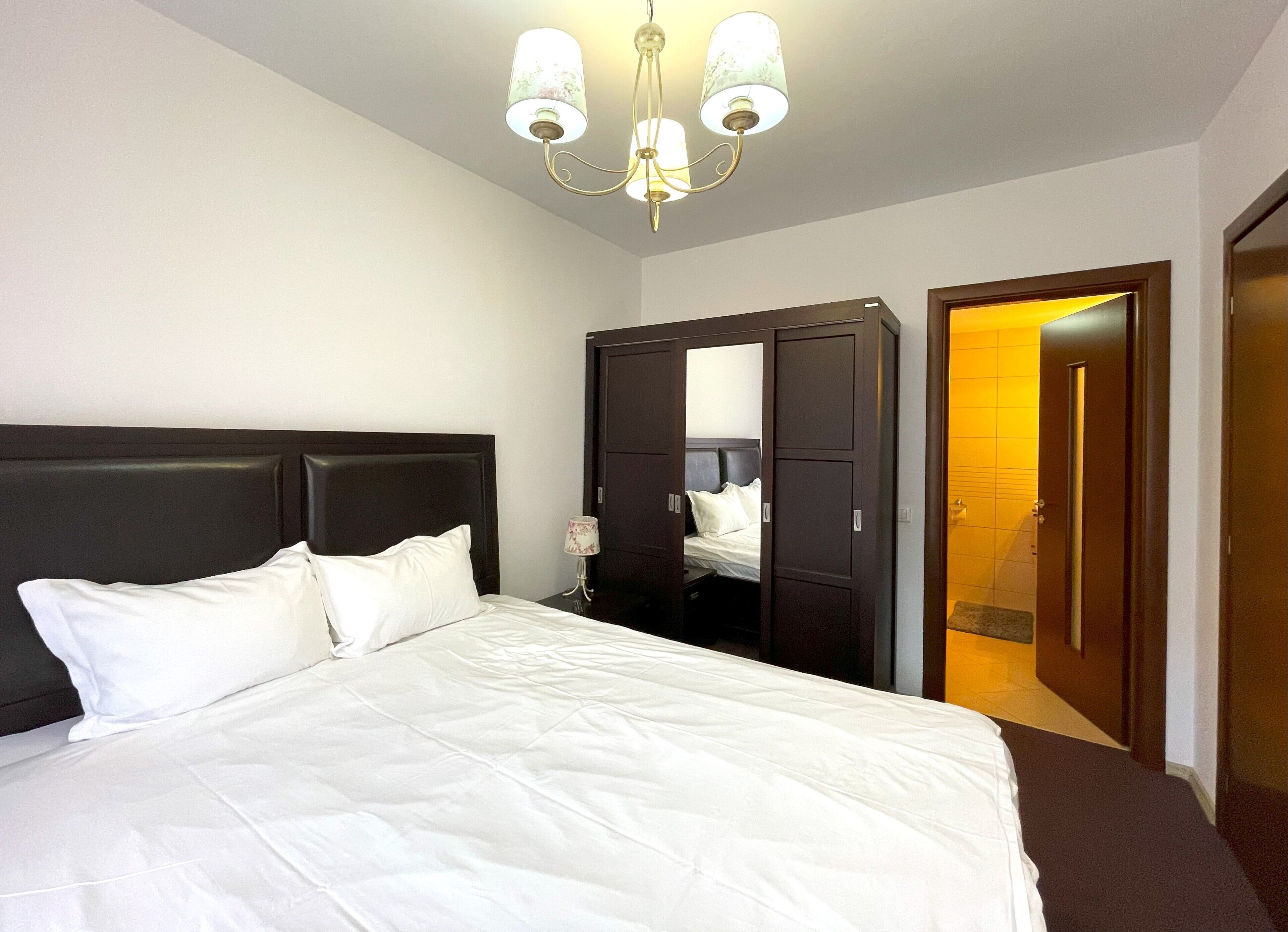 A hotel room with a large bed, a dark headboard, a wardrobe, and a door leading to a bathroom.
