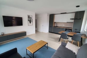 Un salon moderne avec un téléviseur à écran plat, une table basse en bois et un canapé gris.