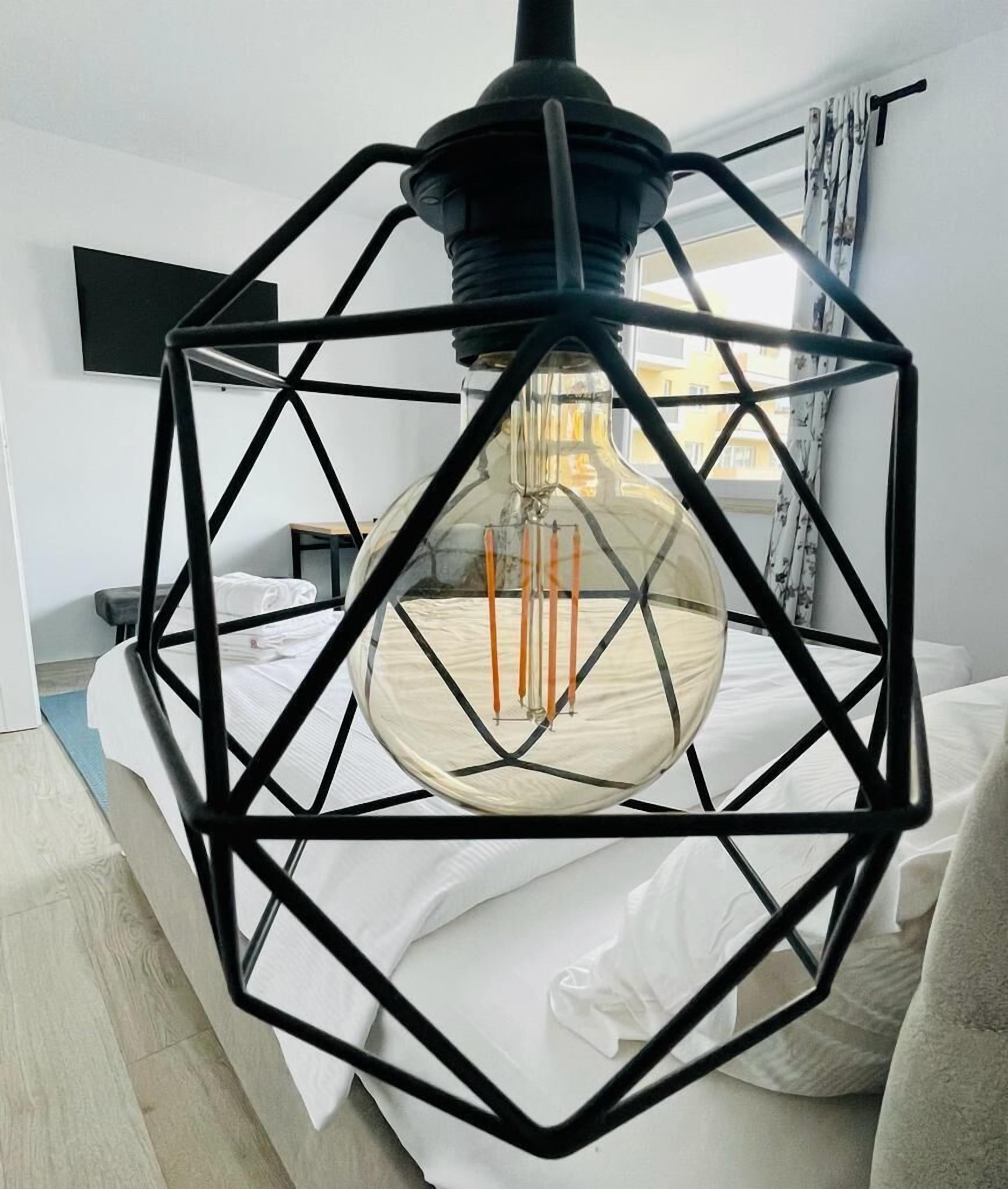 Une pièce moderne agrémentée d’un luminaire géométrique en métal noir et d’une ampoule en verre transparent.