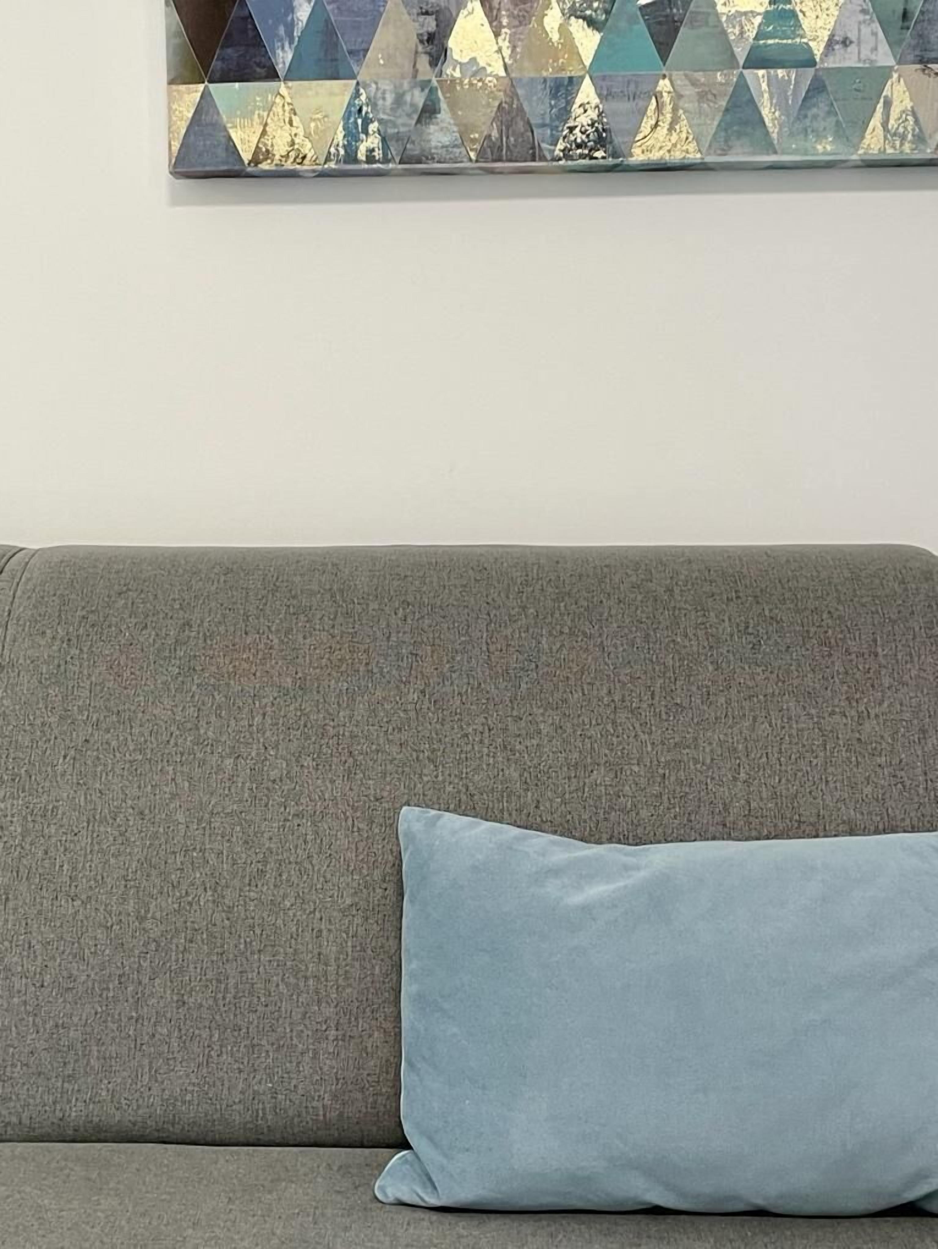 A grey sofa with a light blue pillow against a white wall.