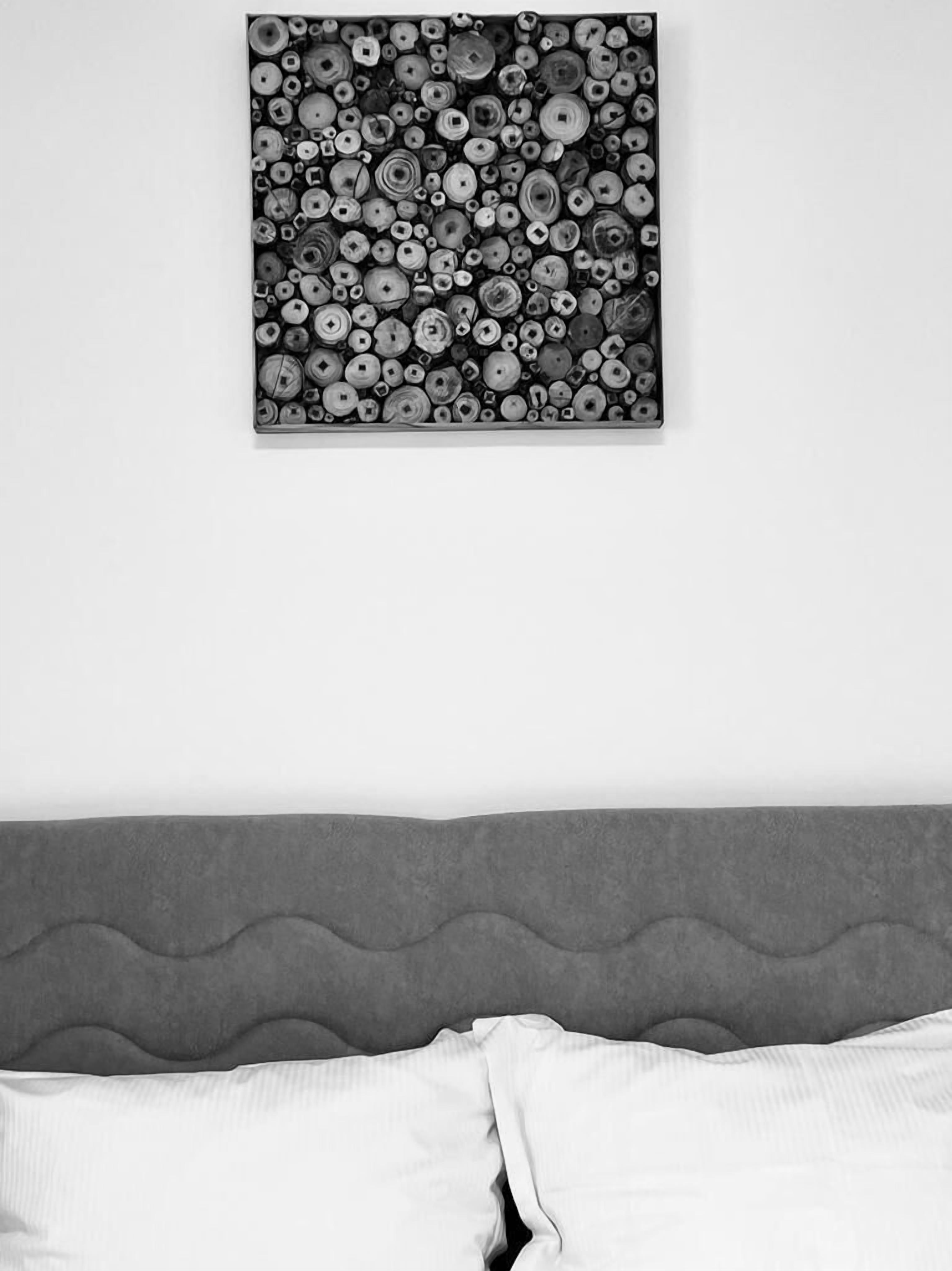 A bedroom with a grey upholstered headboard, a white bedspread, and a black and white abstract art piece on the wall.