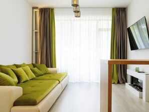 Een moderne woonkamer met een groene bank, een flatscreen televisie en een minimalistisch design.