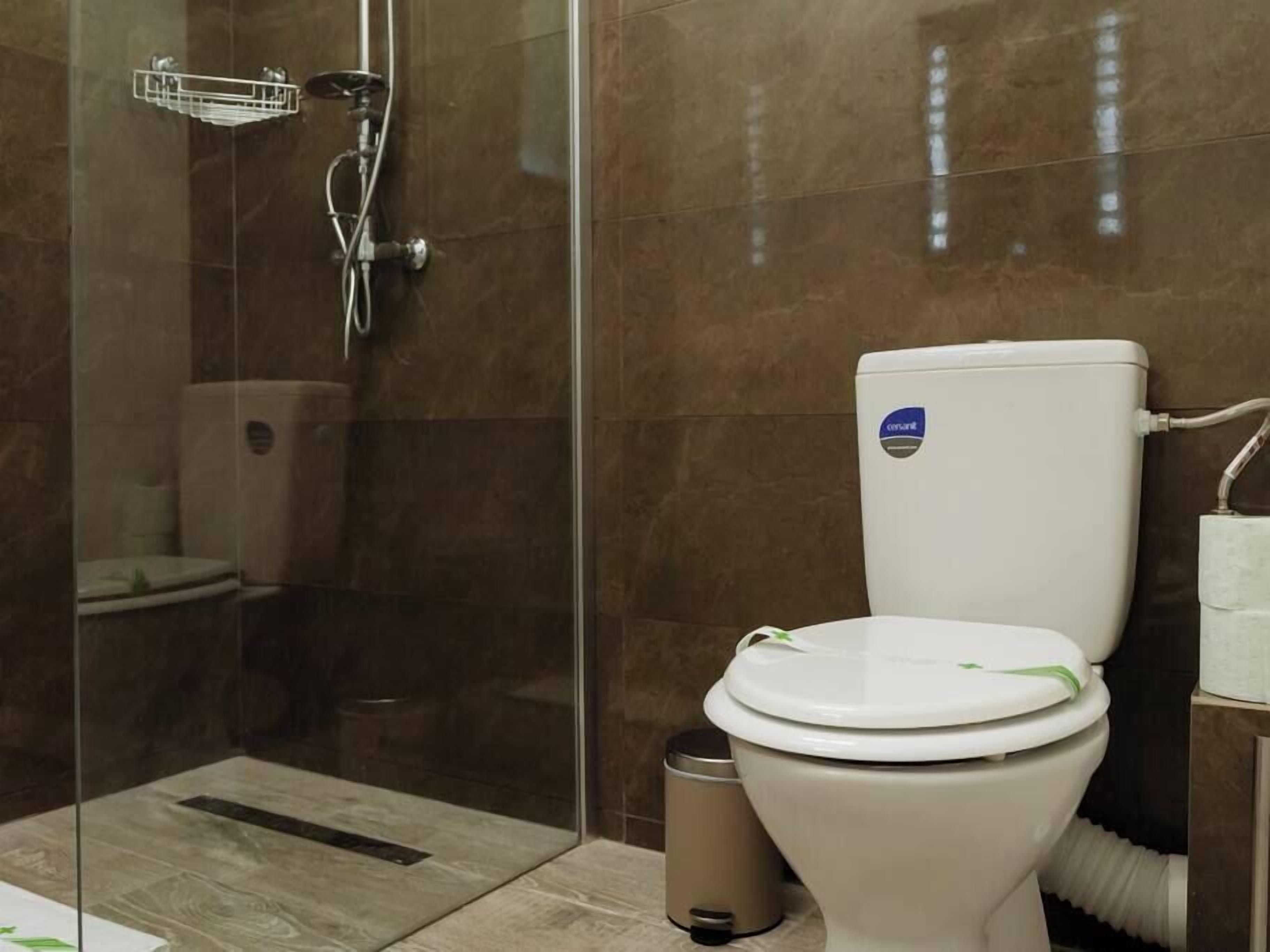 Une salle de bain moderne avec une douche à parois de verre, des toilettes décorées d’un ruban vert et une poubelle.