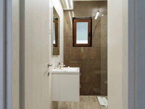 Een moderne badkamer met een witte wastafel, een douchecabine met glazen wanden en een spiegel boven de wasbak.