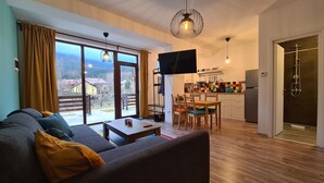 Ett vardagsrum med en soffa, ett matbord och stolar, ett kök med en tv och utsikt över omgivningen.